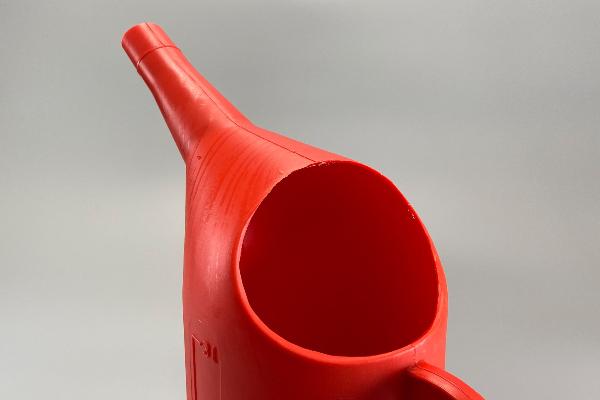 Red plastic jug with a long spout and a handle, with volume markings on the side.